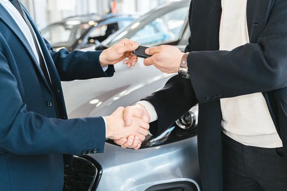 Two people shaking hands while exchanging a car key, illustrating a vehicle handoff
